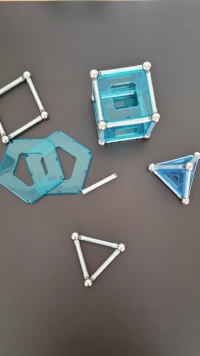 Das Bild zeigt aus magnetischen Stäben, Kugeln und Plastikteilen aus den geometrischen Grundformen Quadrat und Dreieck zusammengebaute geometrische Körper. Die Stangen und Kugeln sind silbern, die Plastikformen in einem durchsichtigem Acrylblau