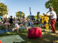 Ein Mann spielt auf einer Wiese Gitarre und singt, links von ihm tanzen Kinder, dahinter sitzen weitere Kinder.