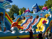 Kinder klettern und rutschen auf einer Hüpfburg mit Delphin- und Hai-Motiven.