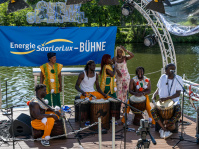 Menschen mit Trommeln und Mikrophonen machen Musik auf einer Bühne, die auf dem Wasser ist.