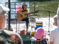 Eine Gitarrenspielerin auf einer Bühne am Wasser.